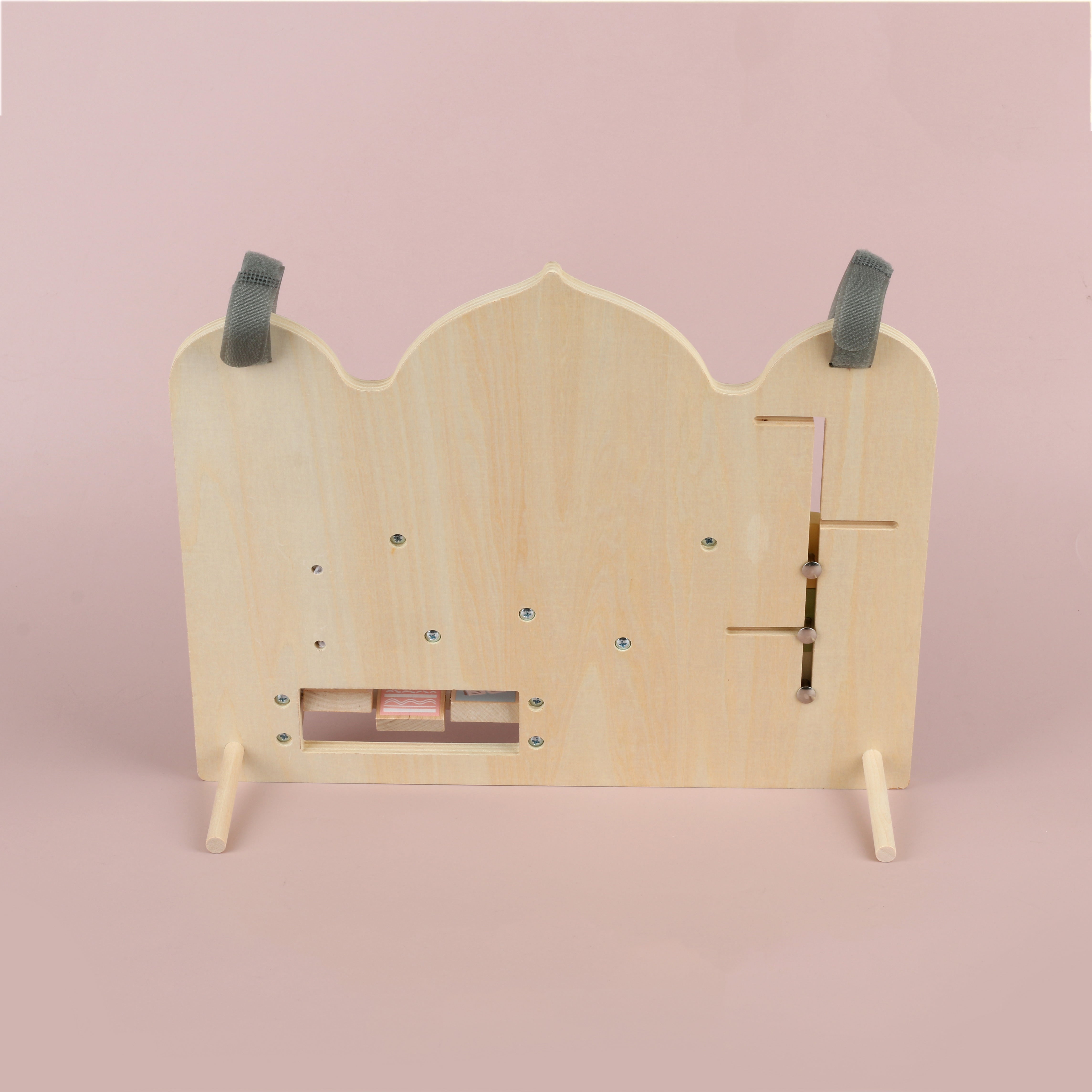 Achterkant van houten activiteitenbord (busy board) met standaard om het bord stevig neer te zetten, Montessori geïnspireerd speelgoed geschikt voor rustig spelen aan tafel of in de speelhoek, duurzame houten constructie met bevestigingen, ontworpen voor open ended play en het oefenen van motoriek en concentratie, voorkant heeft een moskee- of mihrab-vorm met subtiele islamitische inspiratie