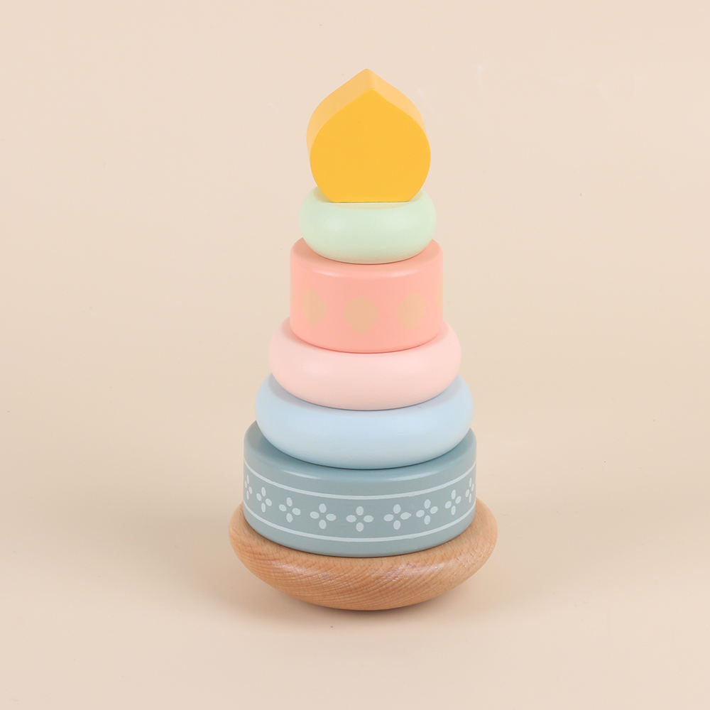 Montessori houten ringstapelaar met losse onderdelen, houten basis met stapelstok en drie grote ringen in pastelroze en lichtblauw met blauwgrijze ring met patroon, daarnaast losse perzikroze ring, mintgroene ring en geel koepelvormig topstuk, educatief peuter speelgoed voor stapelen, grijpen en hand-oogcoördinatie